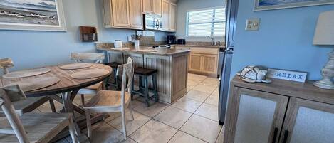 Een keuken met houten kastjes, een eettafel met stoelen, een koelkast en een plafondventilator.