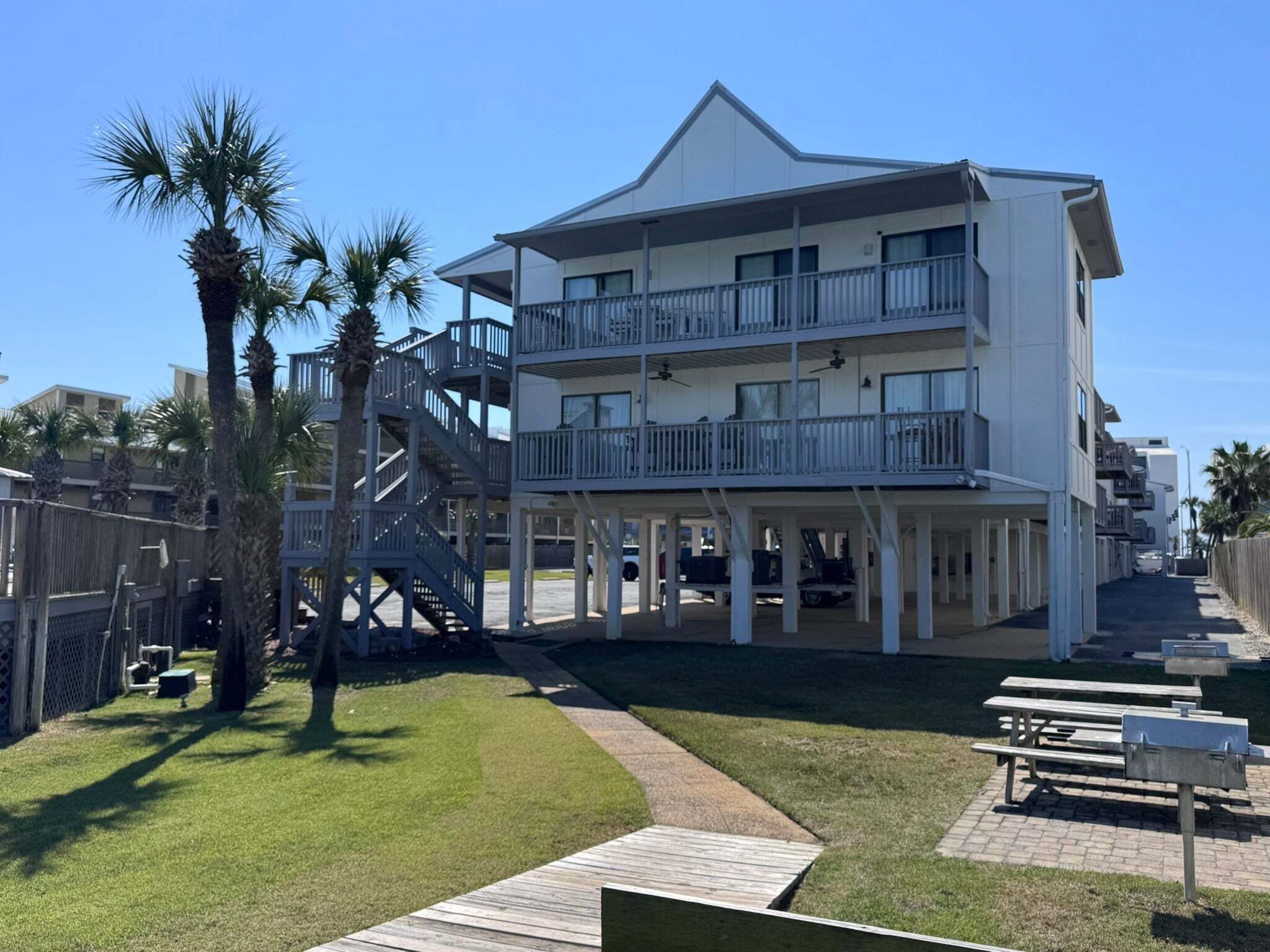 A multi-story building with balconies, a covered walkway, and a grassy area with picnic tables.