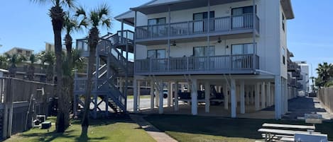 A multi-story building with balconies, a covered walkway, and a grassy area with picnic tables.
