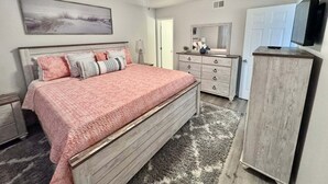 Ein Schlafzimmer mit Bett, Kommode, Spiegel, Deckenventilator und Bildern an der Wand.