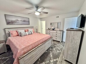Ein Schlafzimmer mit Bett, Kommode, Spiegel, Deckenventilator und Bildern an der Wand.