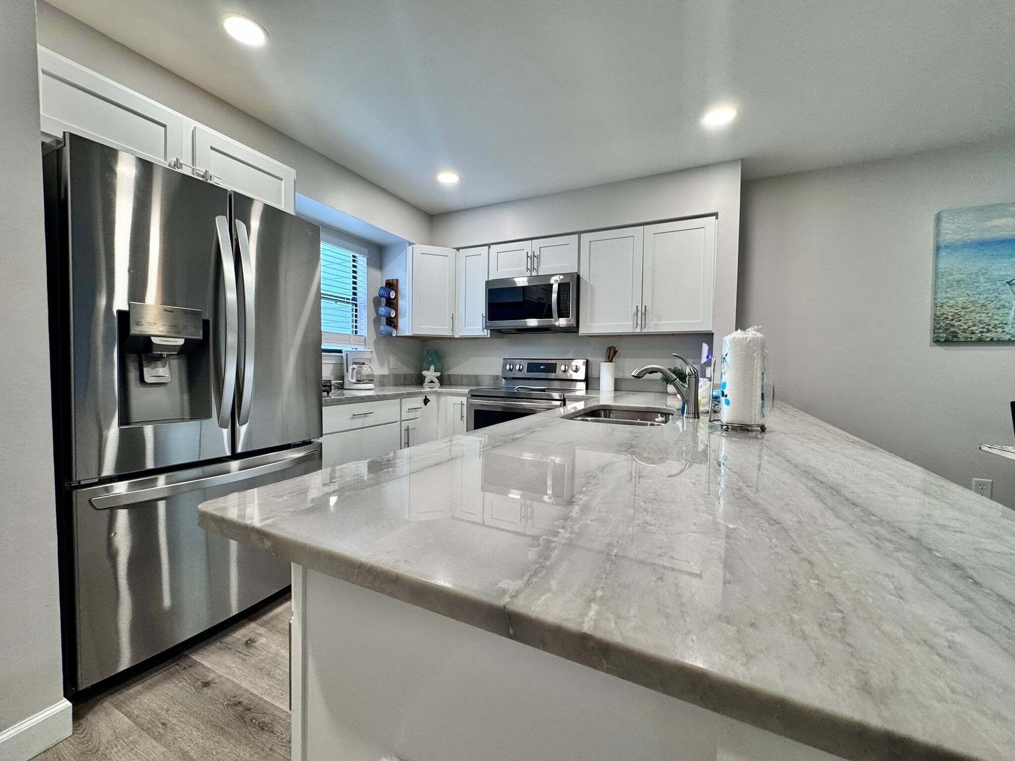 A modern kitchen with stainless steel appliances, white cabinetry, and a marble countertop.