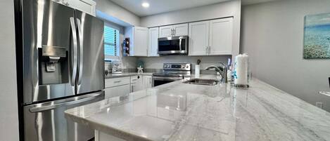A modern kitchen with stainless steel appliances, white cabinetry, and a marble countertop.