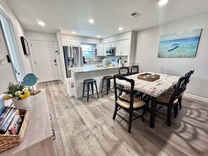 A modern kitchen with white cabinets, stainless steel appliances, and a wooden dining table with four chairs. - Welcome to This 2br/2ba Relaxing Coastal Escape (Orange Beach)
