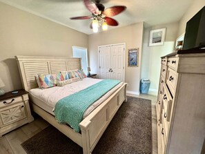 Ein Schlafzimmer mit Bett, Nachttisch, Kommode, Deckenventilator und einer Tür.