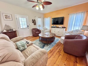 Ein Wohnzimmer mit rundem Couchtisch, Sofas, einem Fernseher und einem Deckenventilator.