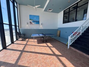 A room with a ping pong table, a chair, a painting, and a staircase. - Welcome to a Beautifully Updated 2br/2ba Gulf-front Escape (Orange Beach)