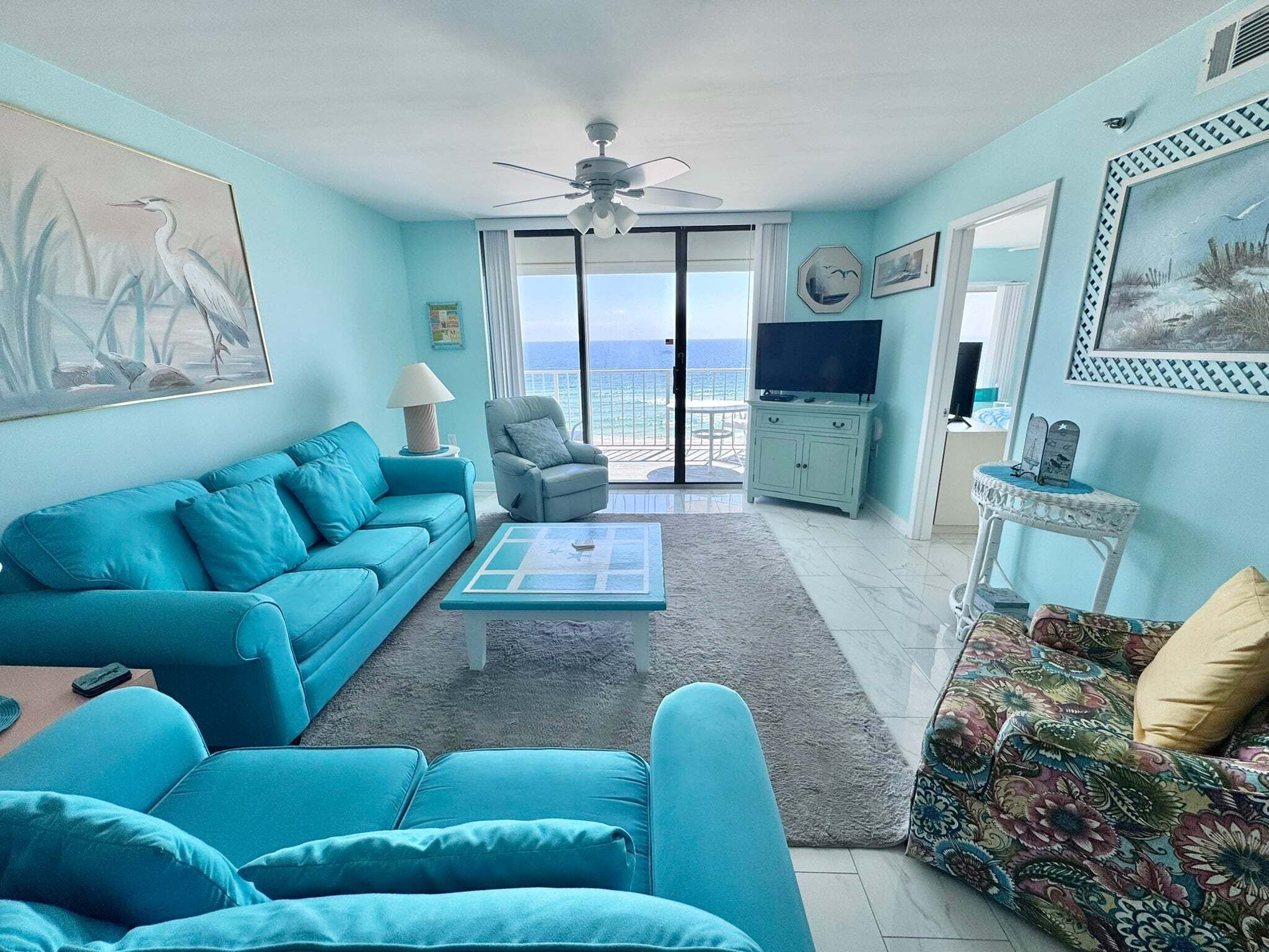 A living room with a sofa, armchair, coffee table, and a view of the ocean through large windows.