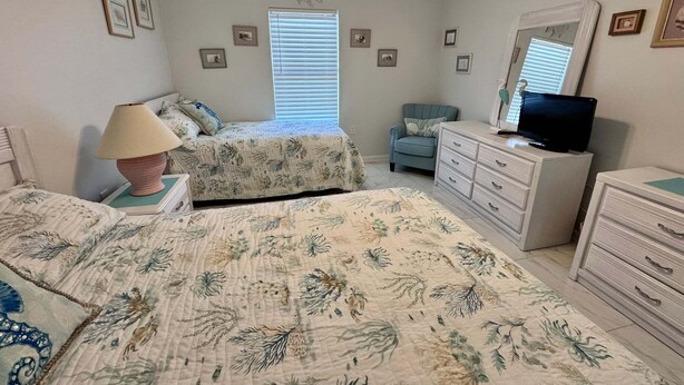A bedroom with two beds, a dresser, a chair, a television, and a ceiling fan. - Welcome to a Beautifully Updated 2br/2ba Gulf-front Escape (Orange Beach)