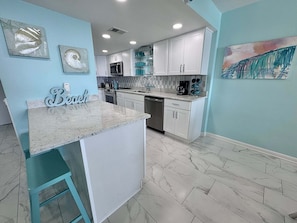 A kitchen with white cabinets, a granite countertop, and a bar stool. - Welcome to a Beautifully Updated 2br/2ba Gulf-front Escape (Orange Beach)