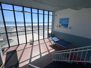 Ein Zimmer mit großen Fenstern, einem Tisch, einem Stuhl und einem Gemälde an der Wand.