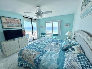 Ein Schlafzimmer mit einem großen Bett, einem Deckenventilator, einem Fernseher und einem Balkon mit Meerblick.