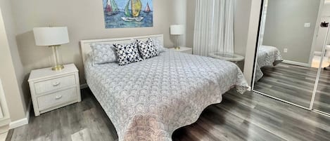 A bedroom with a bed, nightstands, a ceiling fan, a painting, and a mirror.