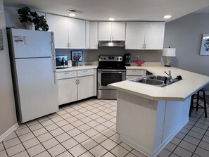 Eine moderne Küche mit weißen Schränken, einem Edelstahl-Kühlschrank, einer Mikrowelle, einem Backofen und einer Spüle.
