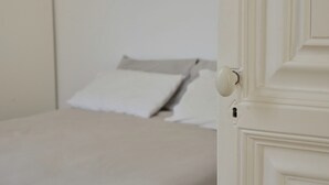 Eine weiße Tür mit einem runden Knopf, die in einen Raum mit einem Bett und einer weißen Wand führt.
