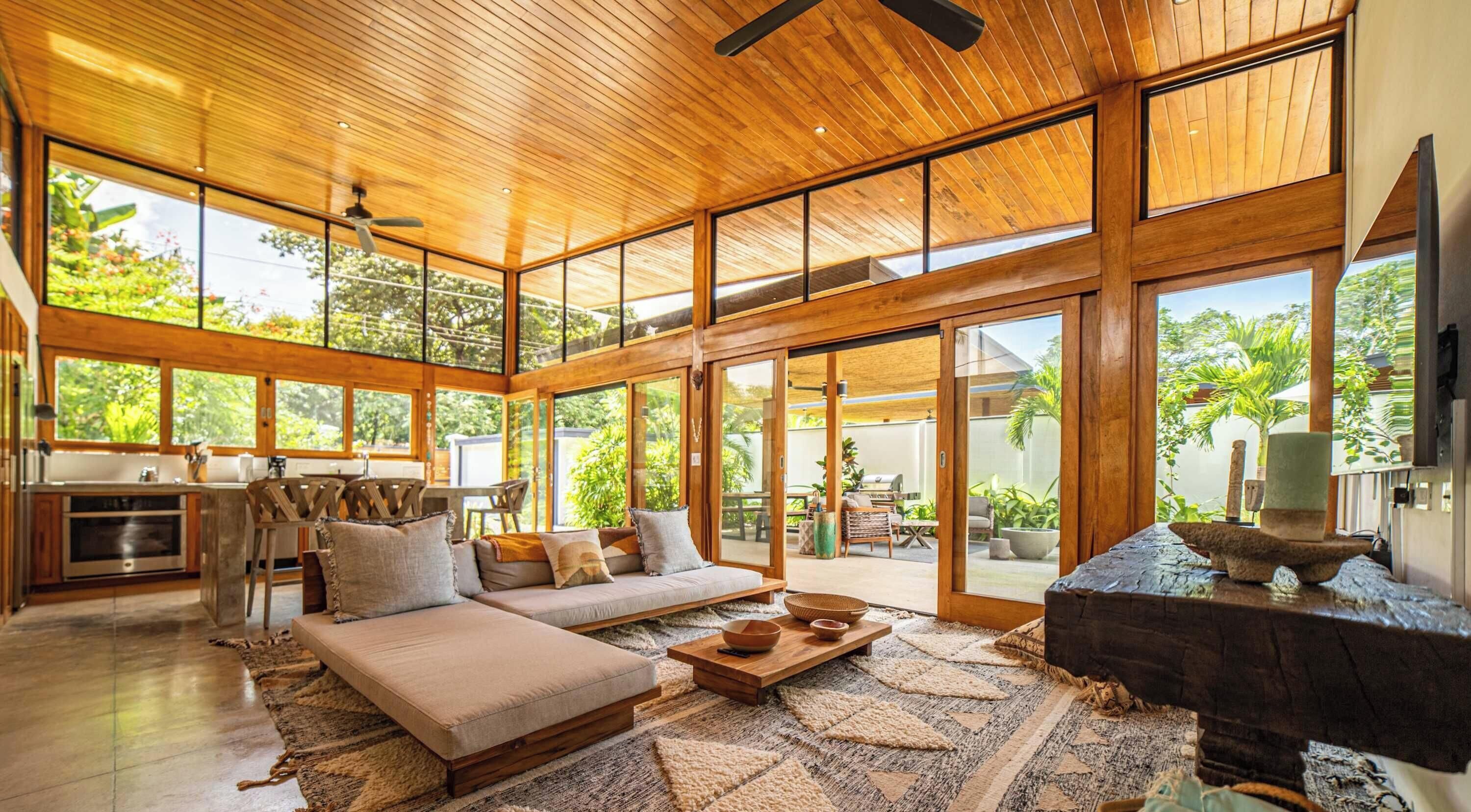 Un espacio habitable amplio con techo de madera, ventanas grandes, un sofá, una mesa de centro y una chimenea.