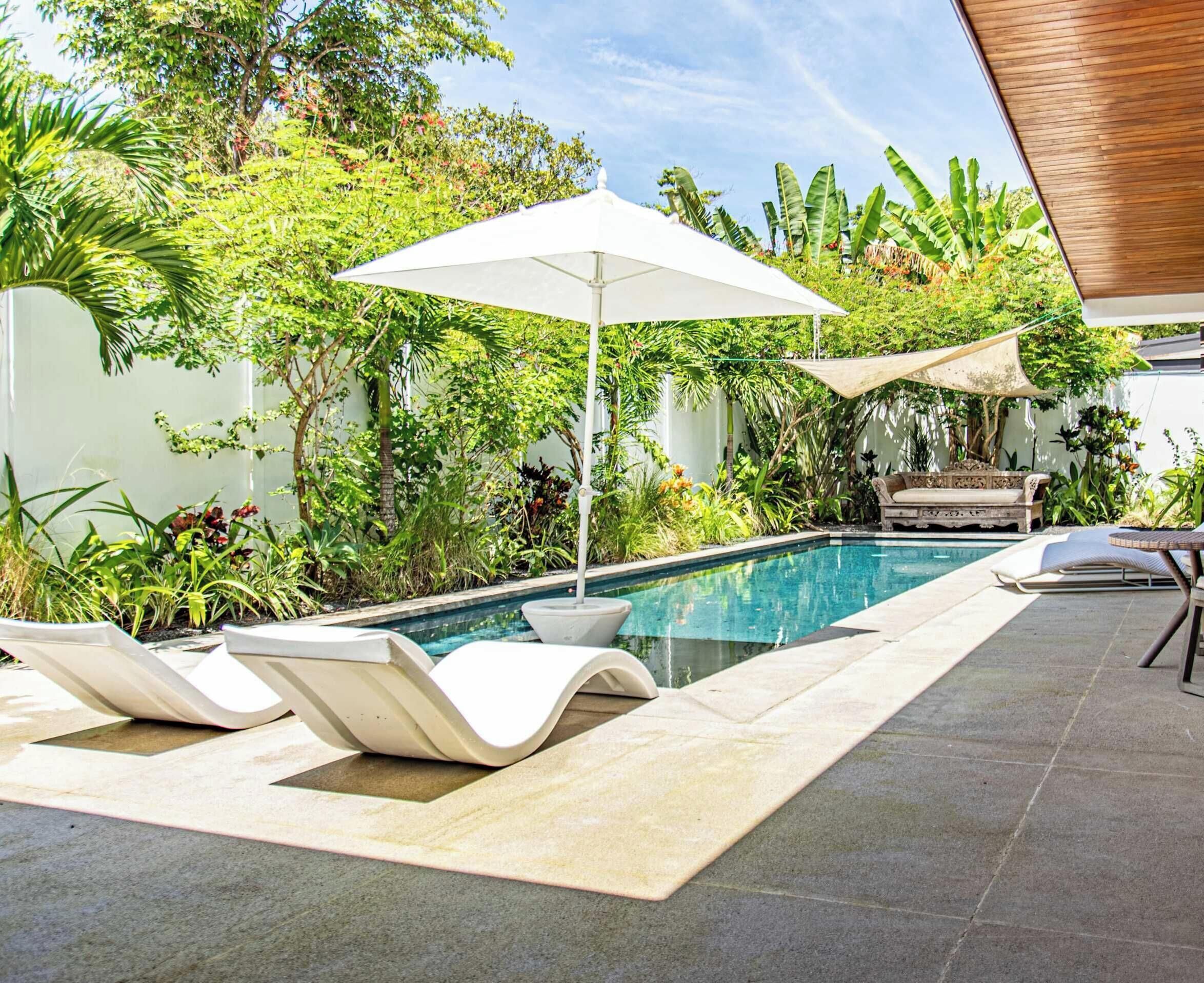 A swimming pool with lounge chairs, surrounded by lush greenery and a wooden pergola.