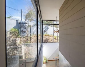 A modern interior with large windows, a staircase, and a hanging light fixture. - Casa del Pez in Playa Pelada (Nosara)