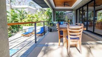 Un espacio de estar techado al aire libre con mesa y sillas, piscina y vistas a la vegetación.
