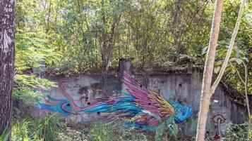 Un mural de un pez colorido sobre una pared de concreto rodeado de follaje.