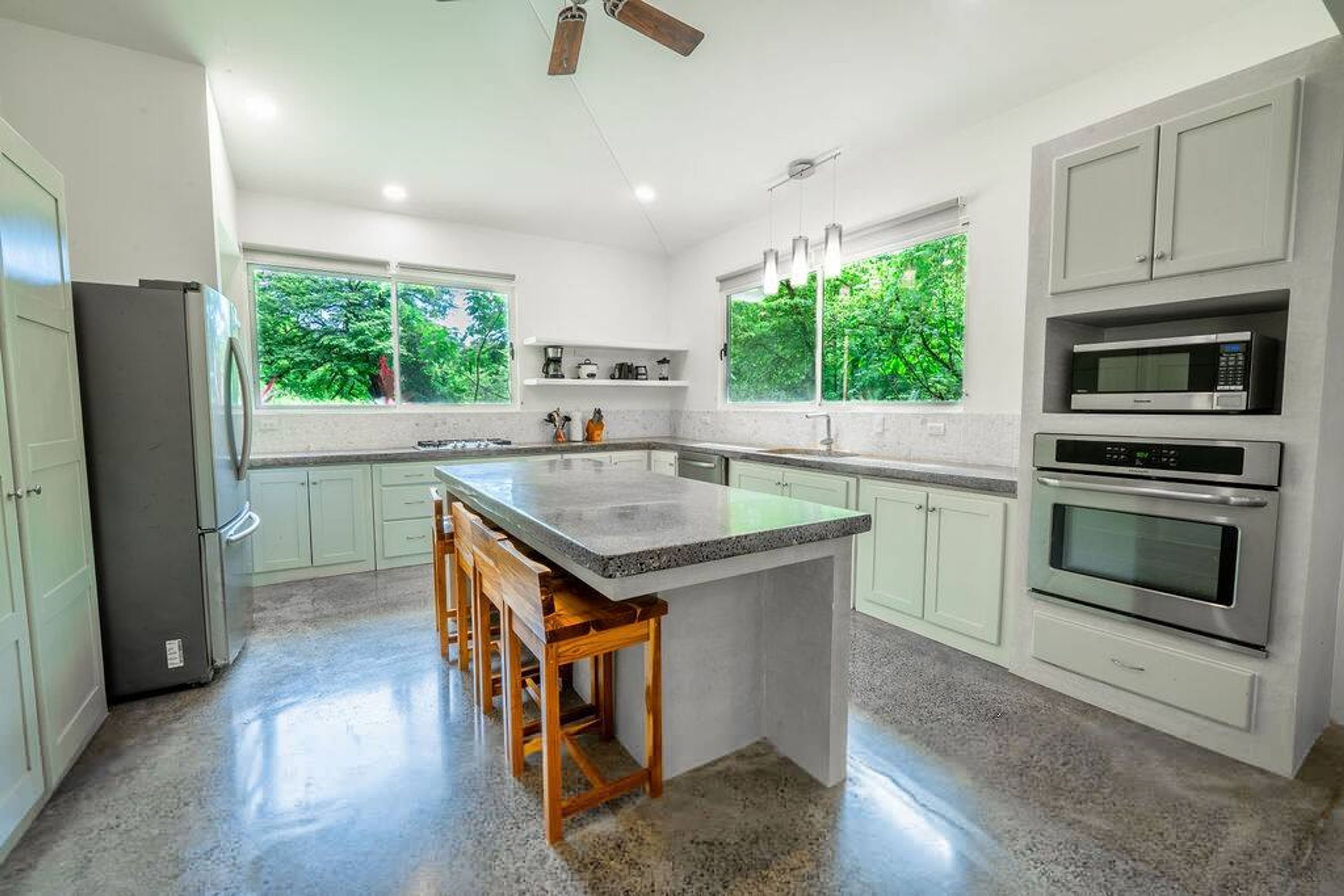 Una cocina moderna con una isla central, electrodomésticos integrados y grandes ventanales con vistas a zonas verdes.