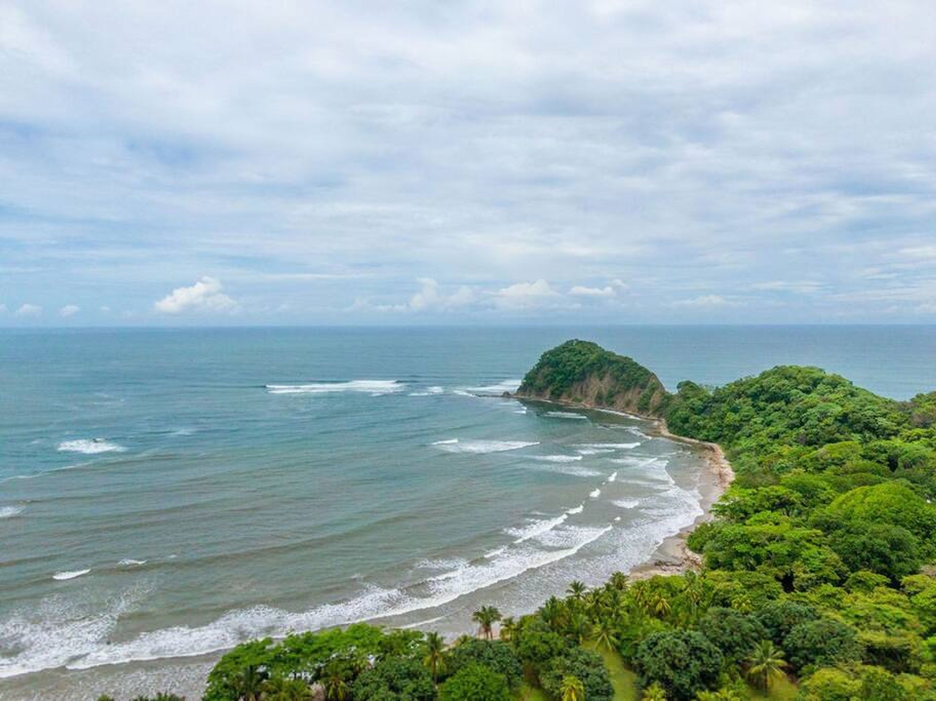 A coastal landscape with a beach, ocean, and lush greenery.