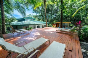 A wooden deck with lounge chairs, a pool, and a house with a green roof. - Spacious 5BR Villa w Saltwater Pool Yoga Deck 4-min Walk to Garza Beach (Nosara)