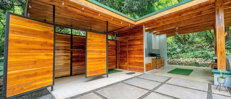 A modern wooden structure with a covered patio area, built-in seating, and a small kitchen area.