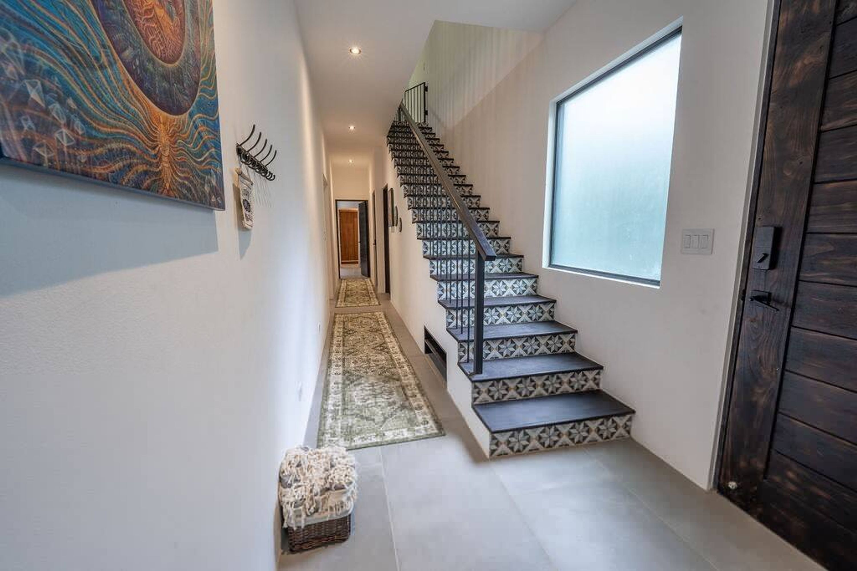 Un escalier moderne, avec des marches à motifs et une rampe, menant à une pièce dotée d’une grande fenêtre et d’une porte en bois foncé.