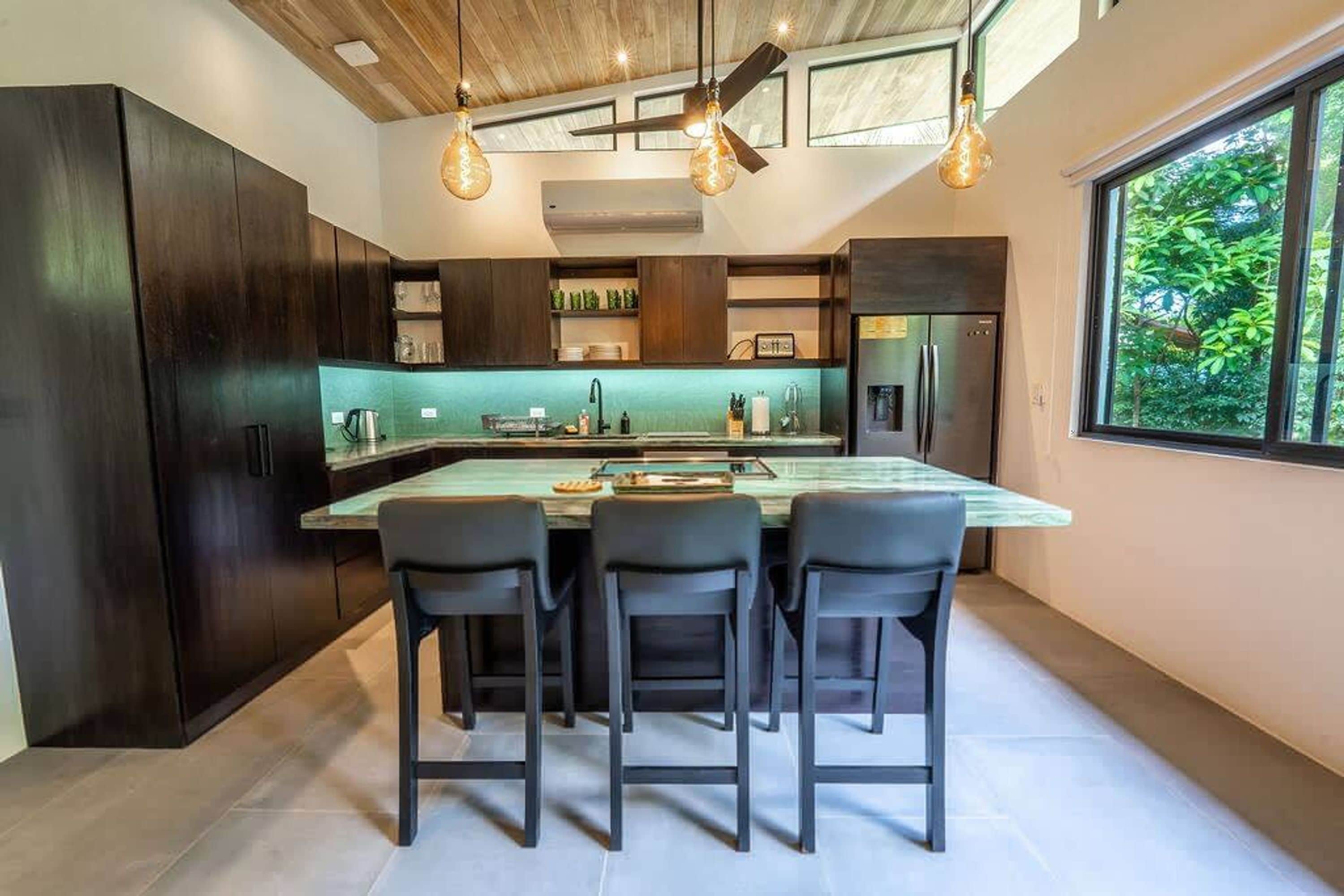 Una cocina moderna con armarios de madera oscura, una isla central con taburetes altos y luminarias colgantes.