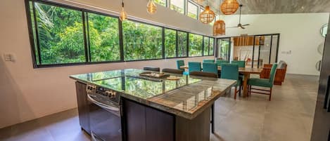 Una cocina moderna con una isla grande, electrodomésticos integrados y ventanas amplias que ofrecen vistas al verdor.