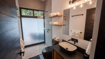 Un baño moderno con un espejo grande, un lavamanos sobre encimera y una cabina de ducha de vidrio.