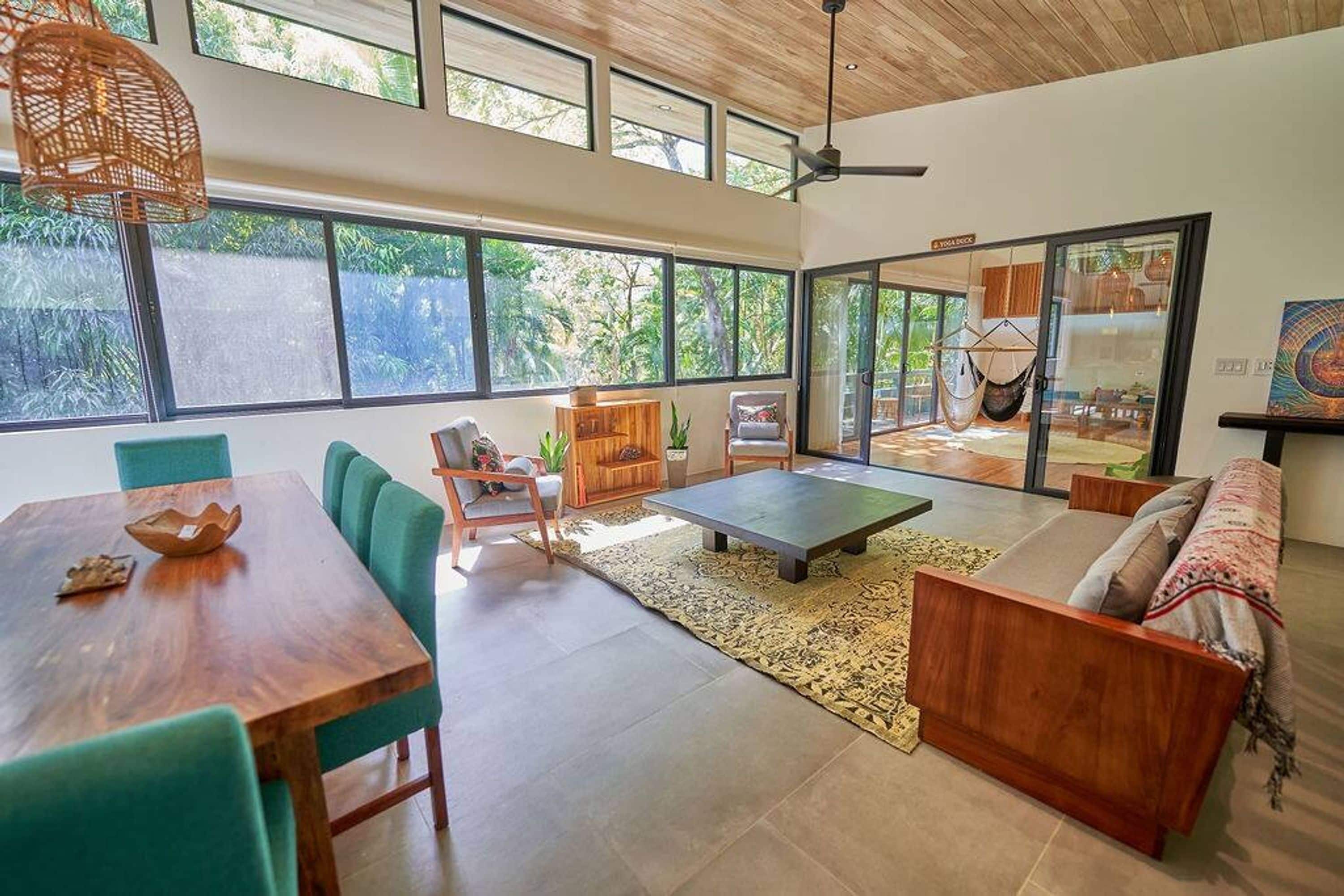 Un salón amplio con una mesa de comedor de madera, sillas verdes, un sofá y una hamaca.