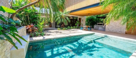 A swimming pool surrounded by lush greenery and a modern building structure.