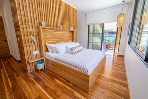 Quarto moderno com cabeceira de madeira, uma cama grande, uma mesinha de cabeceira e uma janela com vista para o exterior.