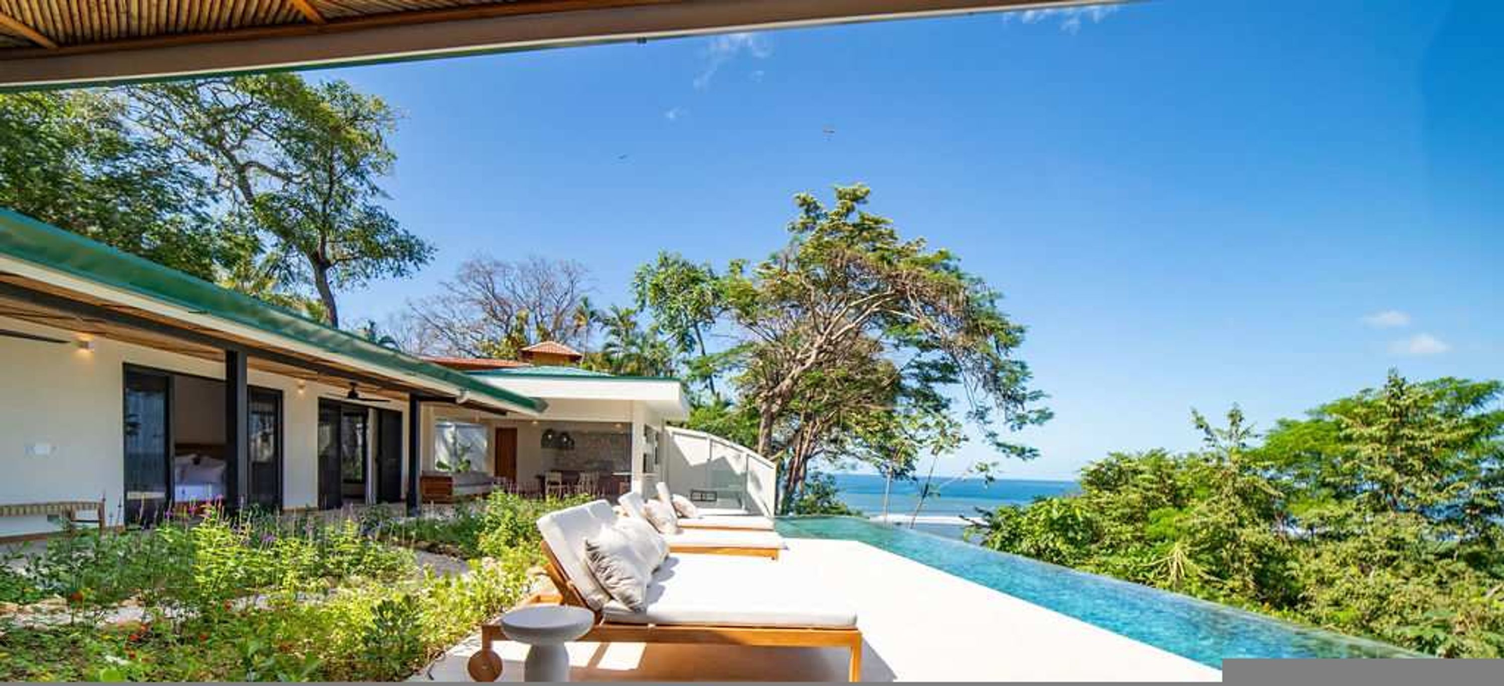 Una villa moderna con piscina, mobiliario exterior y vista al océano.