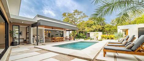 Una casa moderna con piscina, mobiliario exterior y un patio.