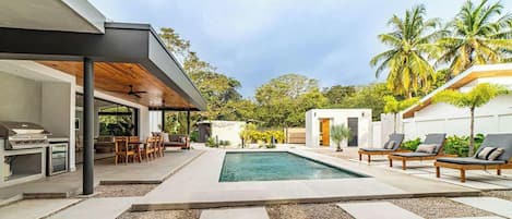 Un espace piscine extérieur moderne, doté d’un coin salon couvert et de chaises longues.