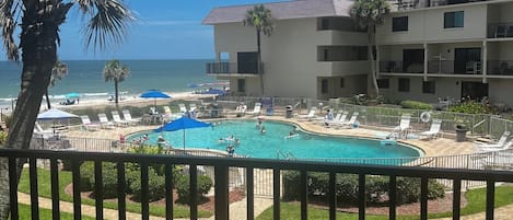 A pool area with lounge chairs and a view of the ocean.