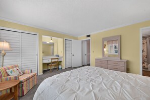 A bedroom with a large bed, a desk, a chair, a dresser, and a mirror. - Quaint Oceanfront Condo (Ormond Beach)