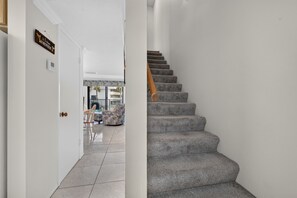 Eine Treppe mit Teppichstufen und einem hölzernen Geländer, die zu einem Raum mit gefliestem Boden und einer Tür mit einem Schild führt.