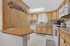 A kitchen with wooden cabinets, a microwave, and a sink. - Quaint Oceanfront Condo (Ormond Beach)