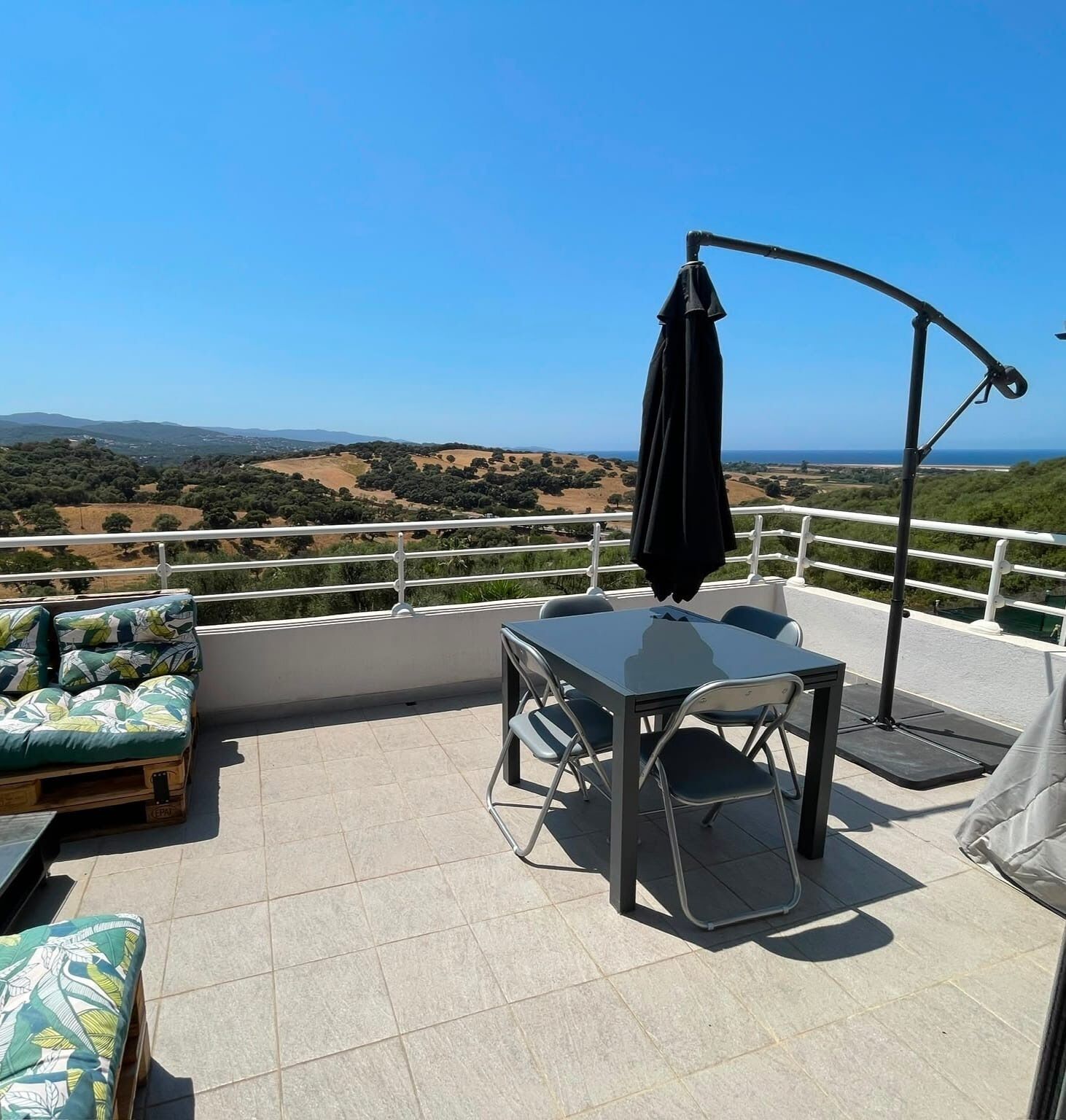 Eine Terrasse mit Tisch und Stühlen, einem schwarzen Sonnenschirm und Blick auf die Landschaft.