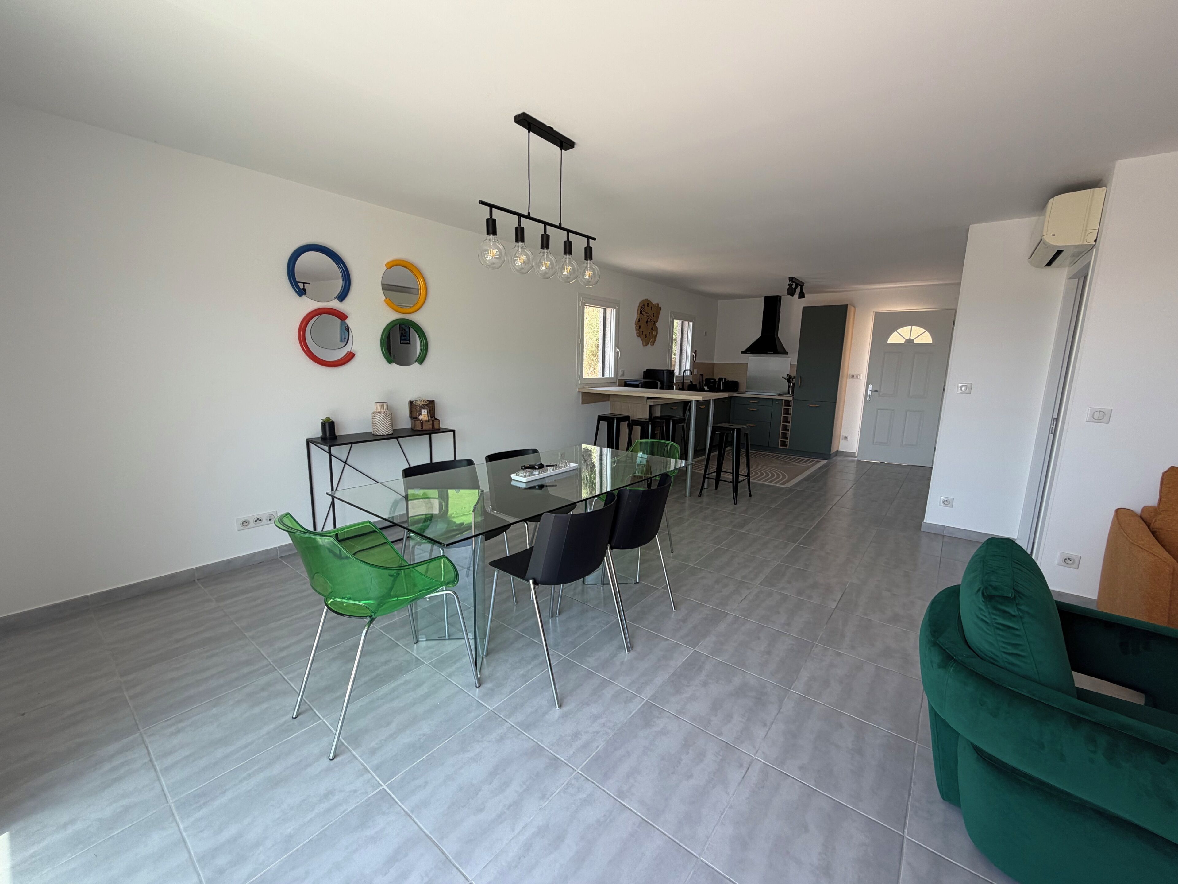 A modern kitchen with a dining area, a green sofa, and a ceiling light fixture.