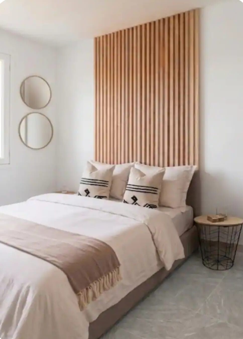 A bedroom with a bed, a headboard, two wall mirrors, and a small round table with a tray.