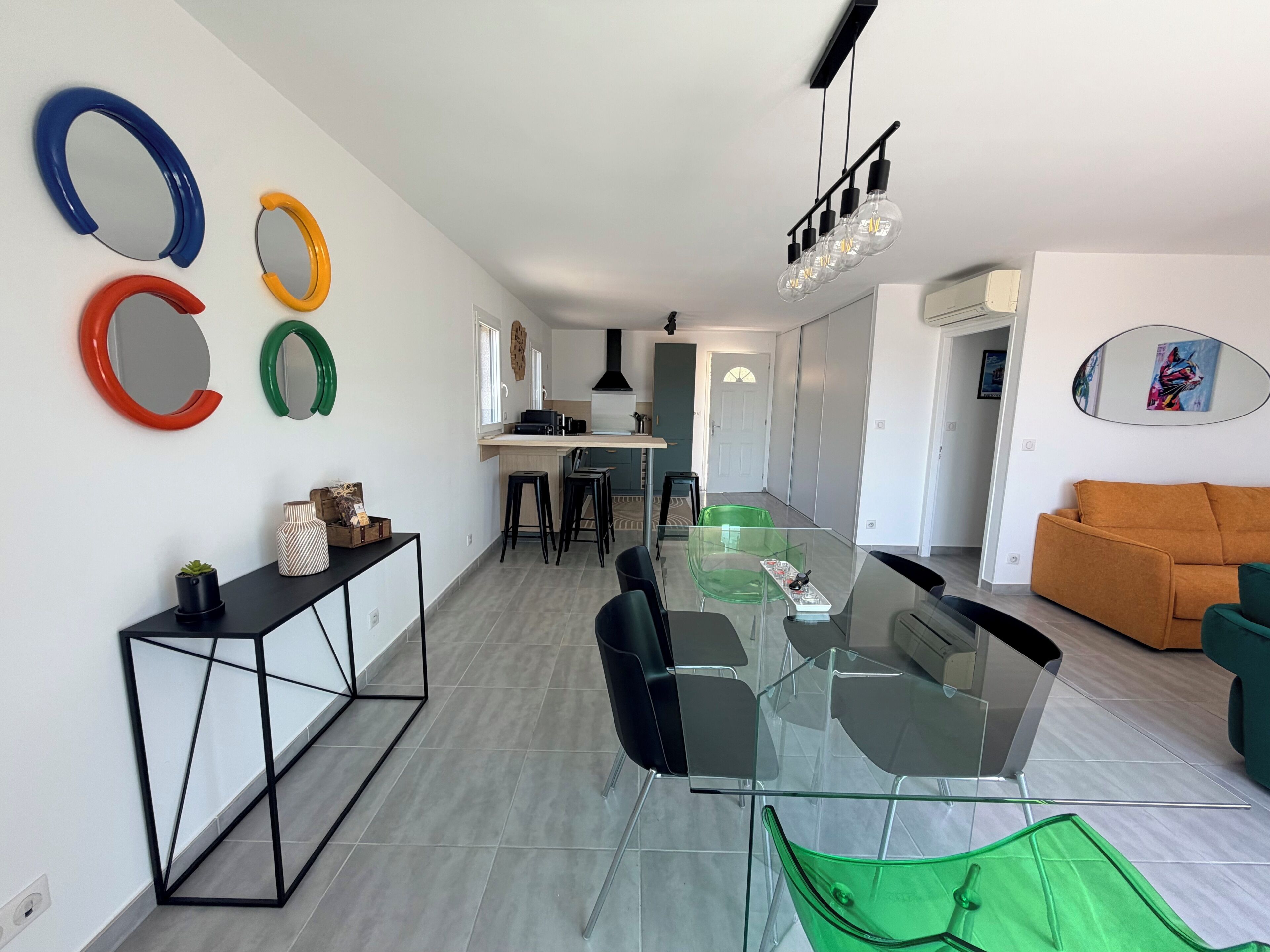Eine moderne Küche mit Kochinsel, ein Essbereich mit Glastisch und Stühlen sowie eine Wohnbereich mit Sofa.