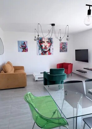 Un salon moderne avec un canapé, des fauteuils, un téléviseur et des œuvres d’art accrochées aux murs.