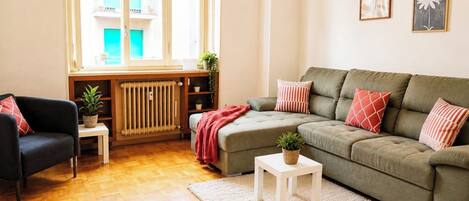 Un salon comprenant un canapé, un fauteuil, un radiateur, une fenêtre et une petite table sur laquelle est posée une plante.