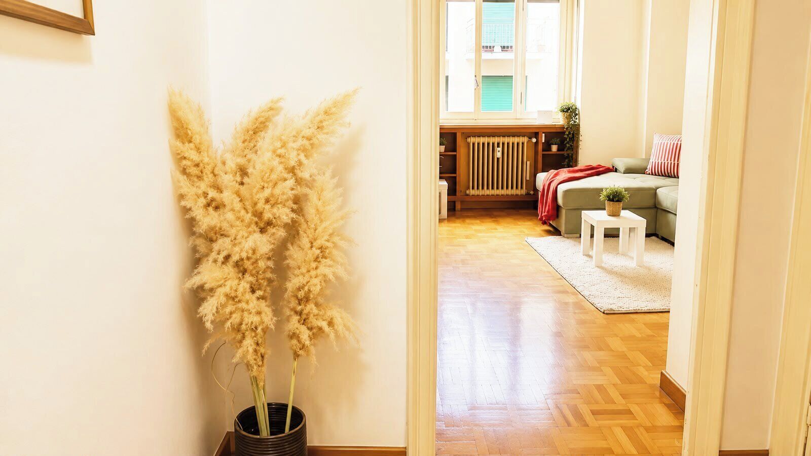 Un couloir mène à un salon où se trouvent un radiateur, un canapé et une petite table.
