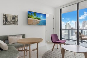 A modern living room with a sofa, a round table, and a chair. There is a large window with a view of a cityscape. - 33rd-Floor City Retreat with Balcony Views in Miami G3308 (Miami Beach)